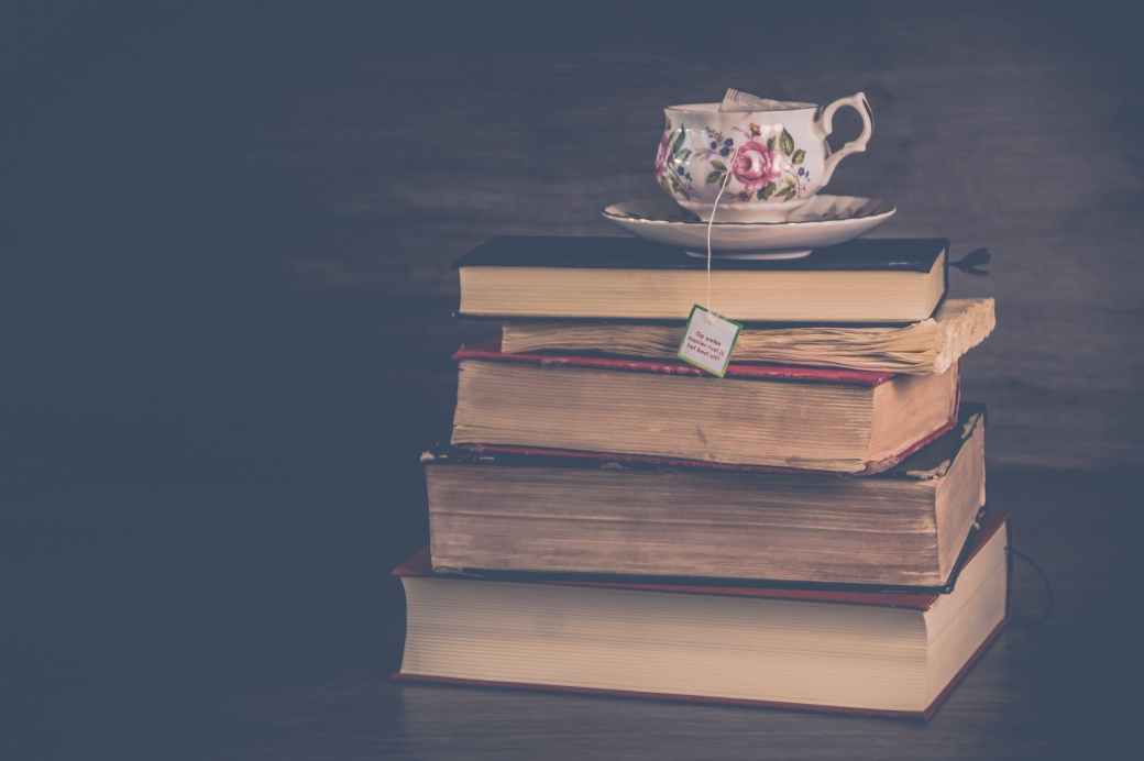 pile of hardbound books with white and pink floral ceramic teacup and saucer